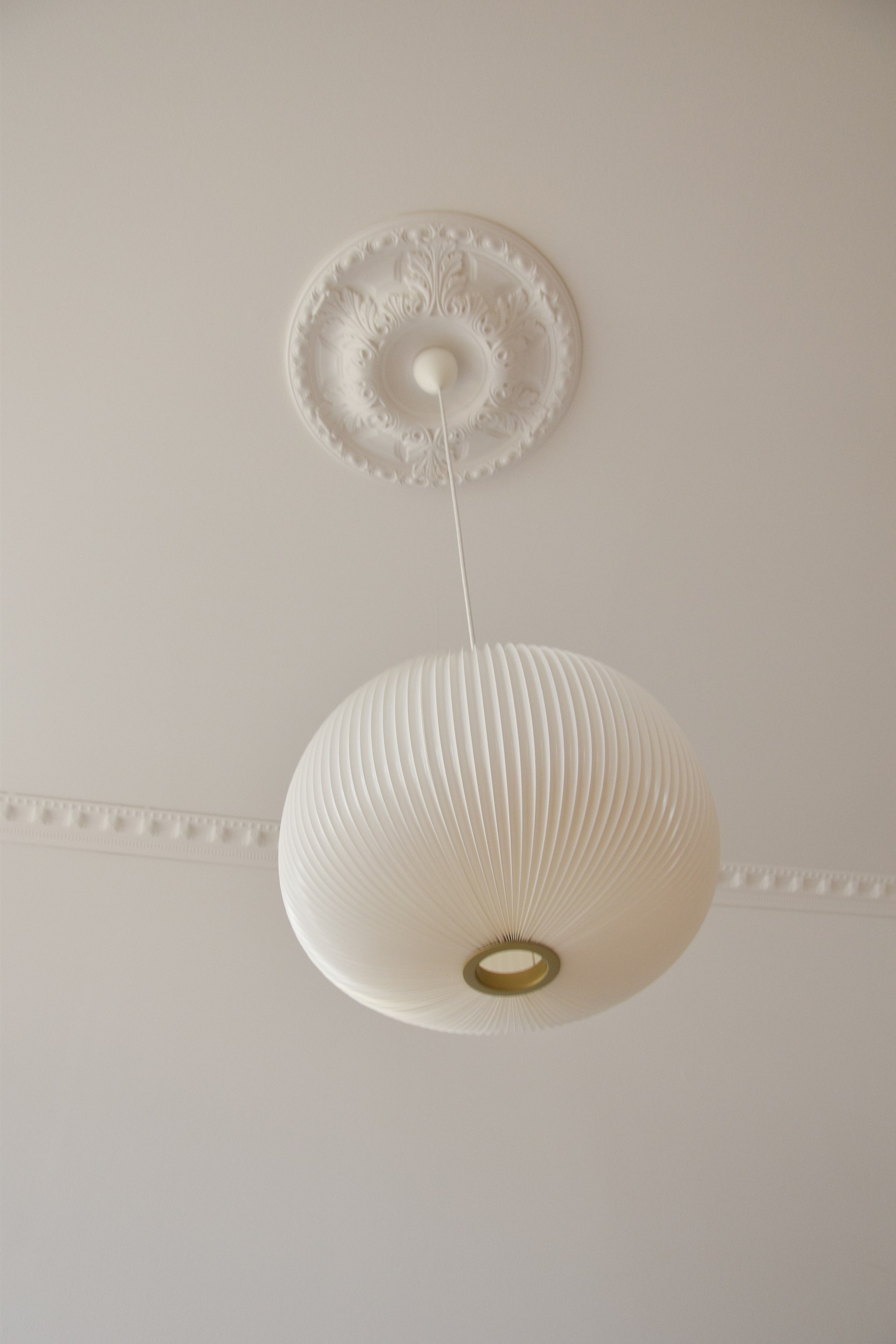 Un rosetón de techo ornamentado que enmarca una lámpara colgante, combinado con molduras de techo discretas para crear una elegante decoración del techo.