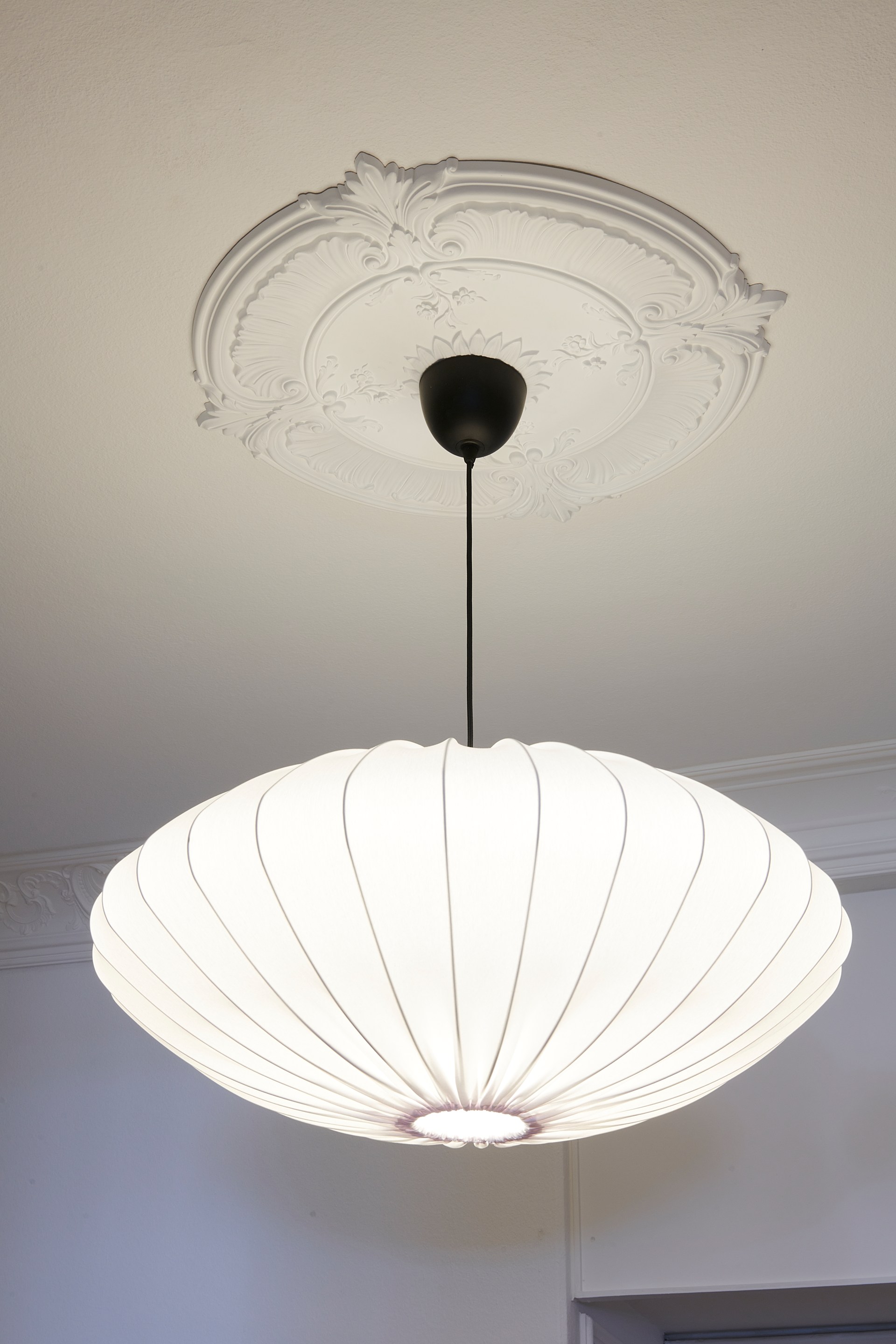 Rosetón de techo ornamentado con detalles esculpidos, combinado con una lámpara colgante para realzar la decoración clásica del techo.